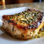 Close-up of a perfectly cooked Crispy Air Fryer Pork Chop topped with glistening garlic butter and herbs.