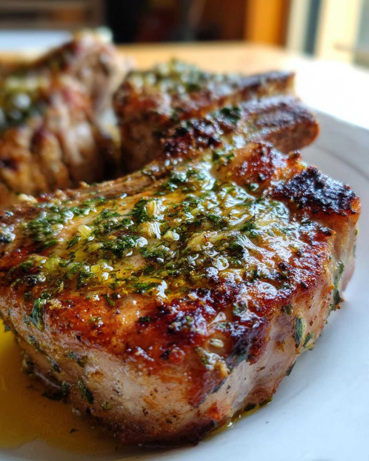 Close-up of a juicy, crispy air fryer pork chop topped with glistening garlic butter and herbs.