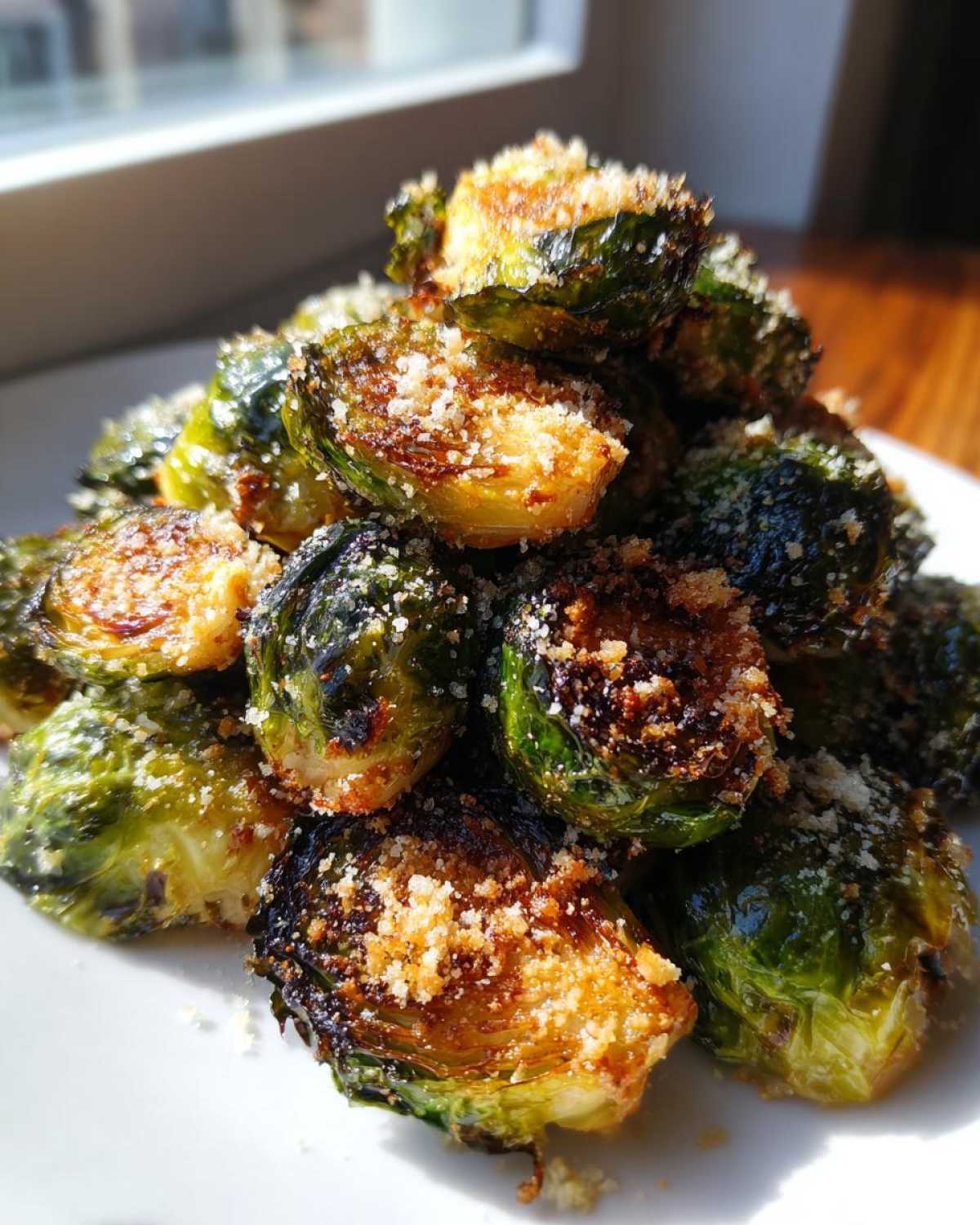 A close-up pile of roasted Crispy Parmesan Brussels Sprouts, showing charred edges and a generous topping of grated cheese.