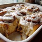 Close-up of warm Gluten-Free Cinnamon Rolls baked together in a white dish, generously covered in white cream cheese icing.