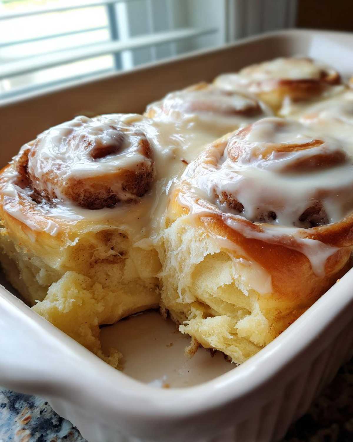Close-up of soft, fluffy Gluten-Free Cinnamon Rolls covered in white icing in a baking dish.