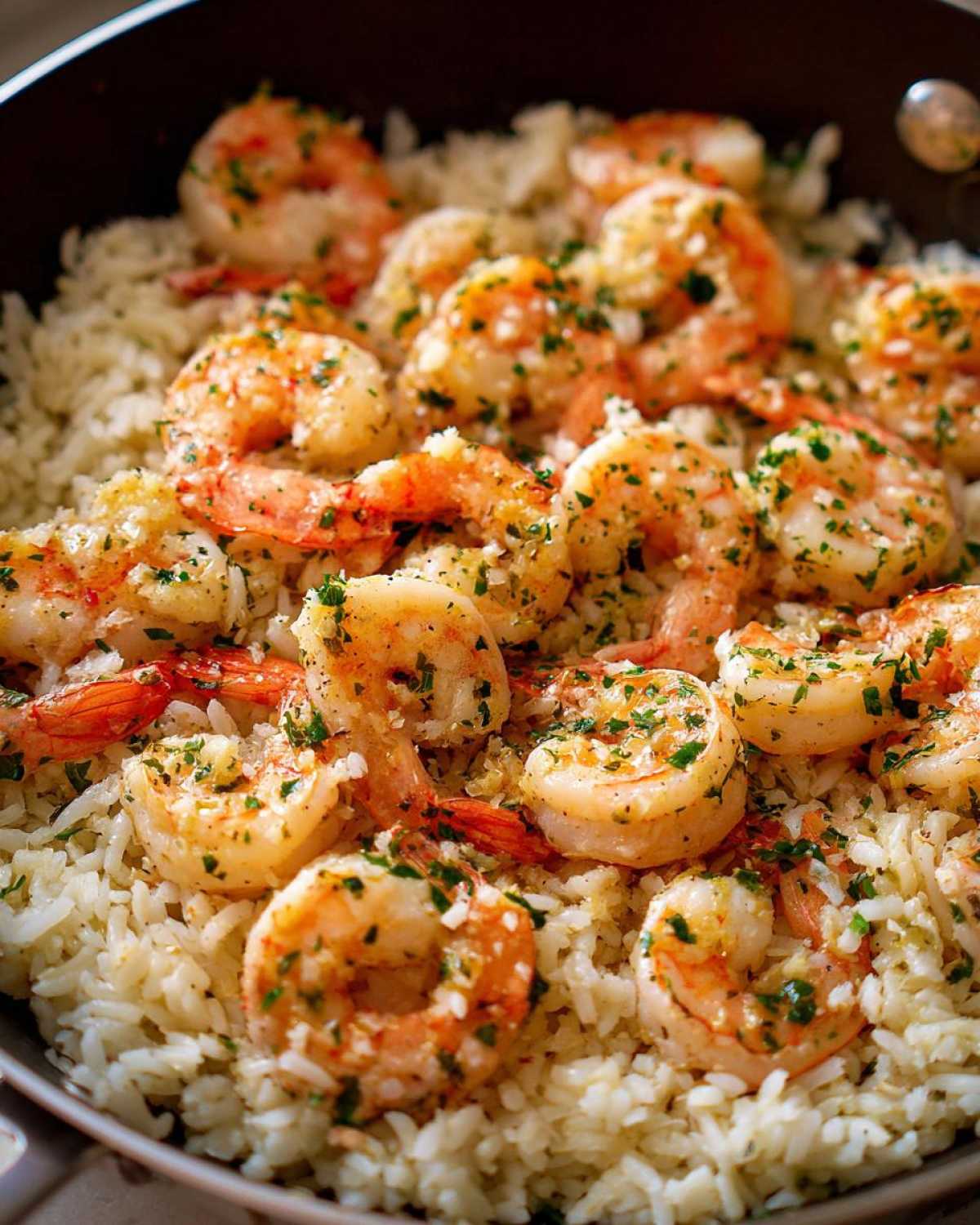 Close-up of plump shrimp coated in garlic butter and parsley served over white rice in a skillet.