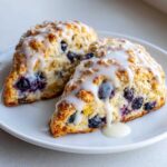 Two triangular Blueberry Lemon Scones topped with thick white glaze, served on a white plate.
