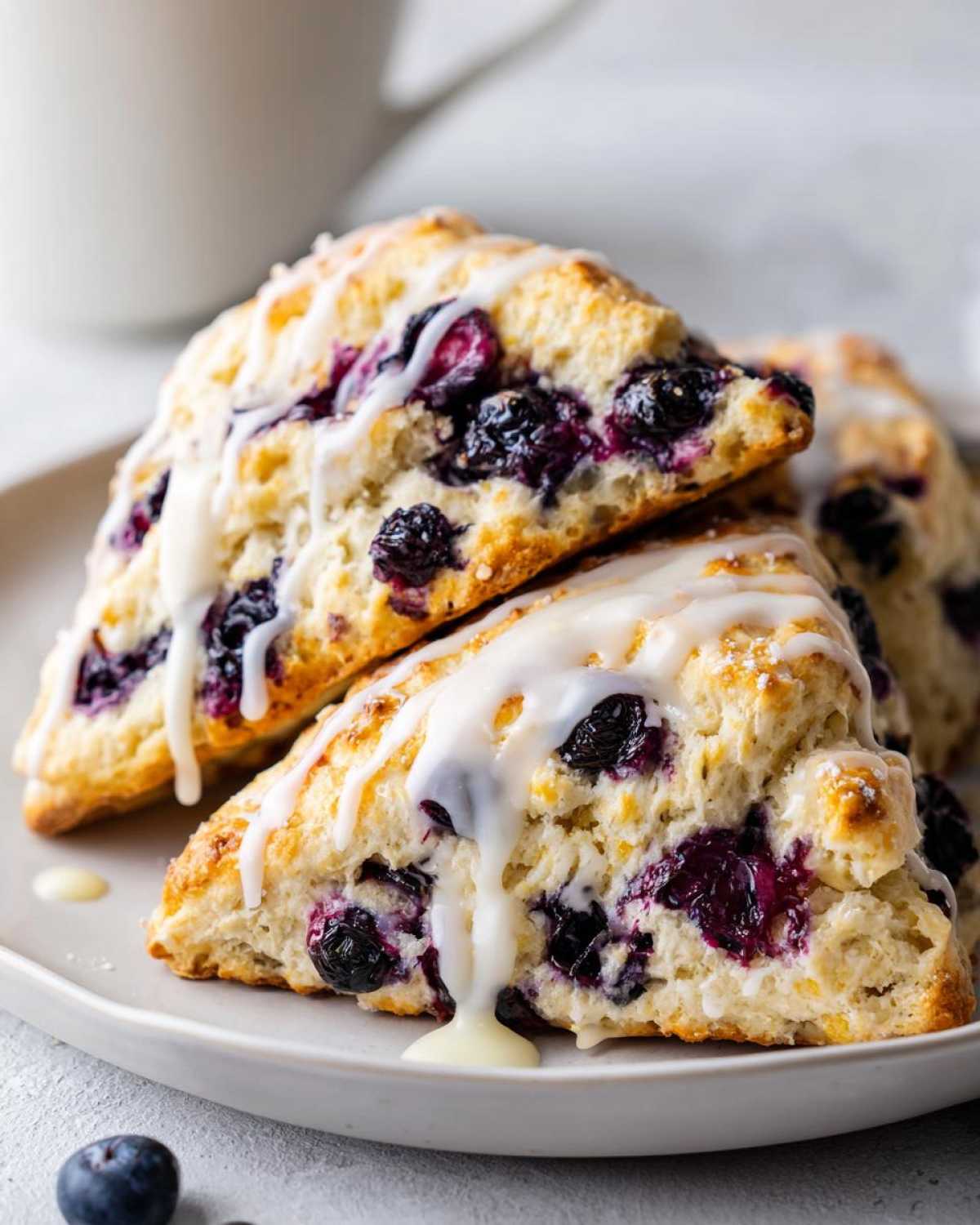 Close-up of two stacked Blueberry Lemon Scones drizzled heavily with white lemon glaze.