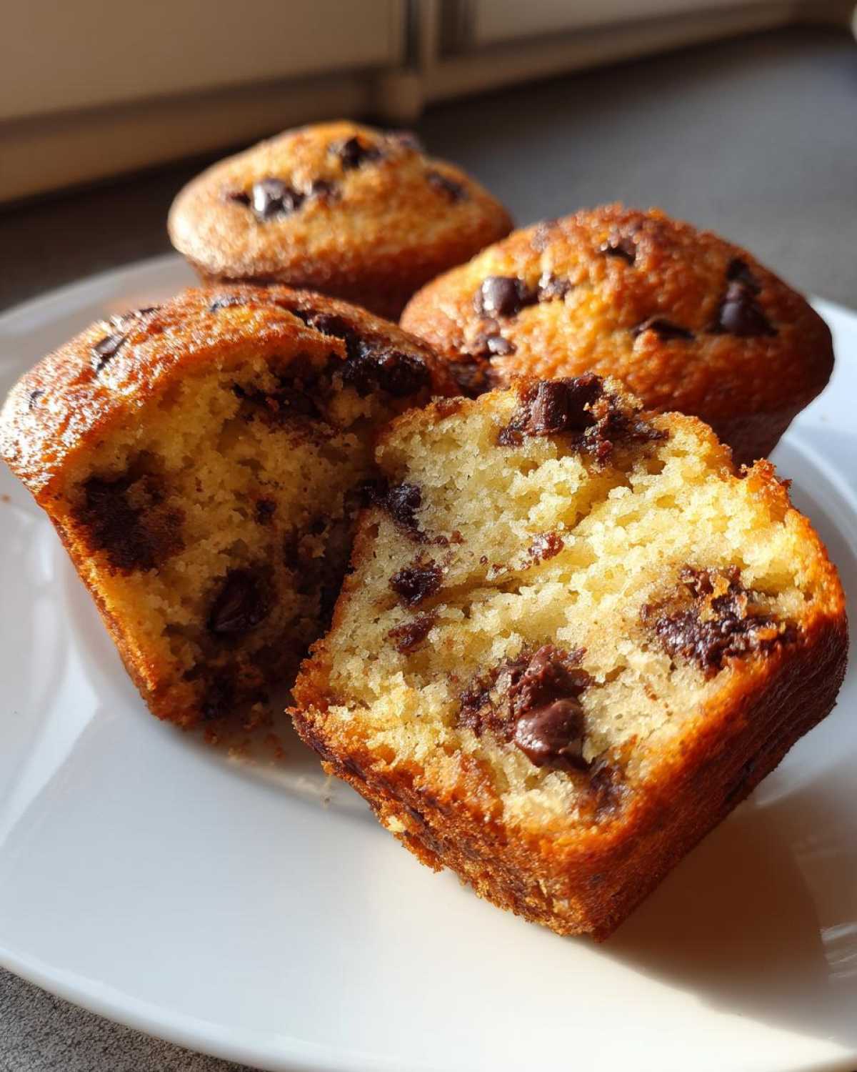 Close-up of moist Gluten-Free Banana Chocolate Chip Muffins, one split open to show the soft interior and chocolate chips.