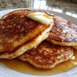 A stack of three golden-brown Gluten-Free Buttermilk Pancakes topped with melting butter and drizzled with syrup.