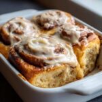 Close-up of four freshly baked Gluten-Free Cinnamon Rolls topped with thick white icing in a white baking dish.