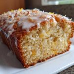 Close-up of a moist Gluten-Free Lemon Coconut Cake loaf topped with white glaze, shredded coconut, and lemon zest.