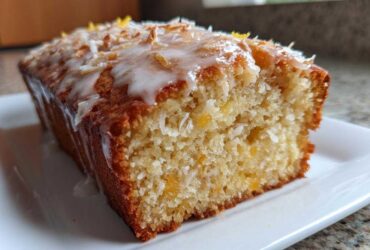 Close-up of a moist Gluten-Free Lemon Coconut Cake loaf topped with white glaze, shredded coconut, and lemon zest.