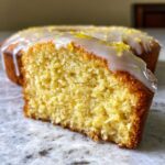 Close-up of a moist slice of Gluten-Free Lemon Coconut Cake topped with white glaze and lemon zest.