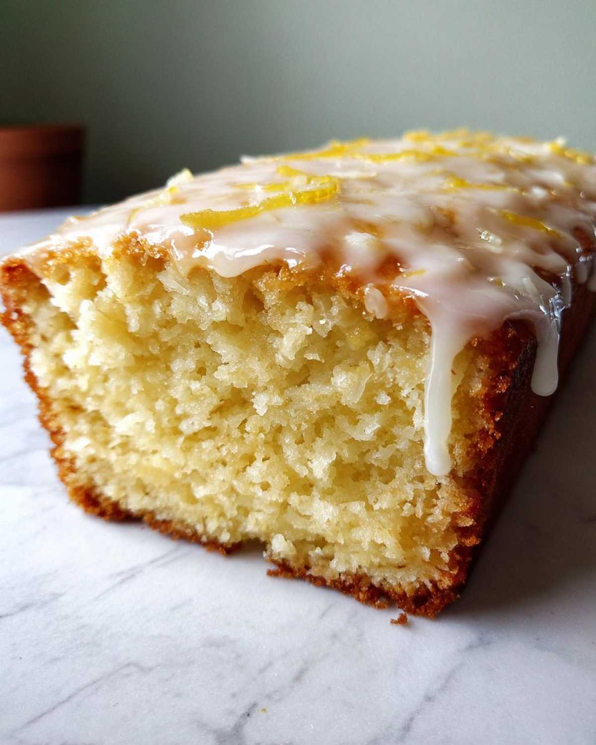 Close-up of a slice of moist Gluten-Free Lemon Coconut Cake with white lemon glaze and zest.