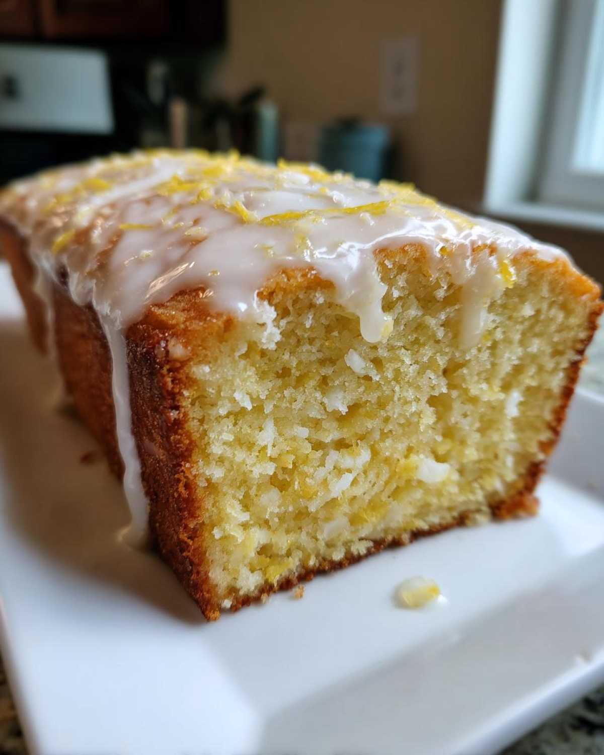 Close-up of a slice of moist Gluten-Free Lemon Coconut Cake drizzled with white glaze and lemon zest.