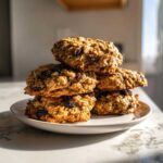 A stack of five thick, chewy Gluten-Free Oatmeal Raisin Cookies piled high on a small white plate.