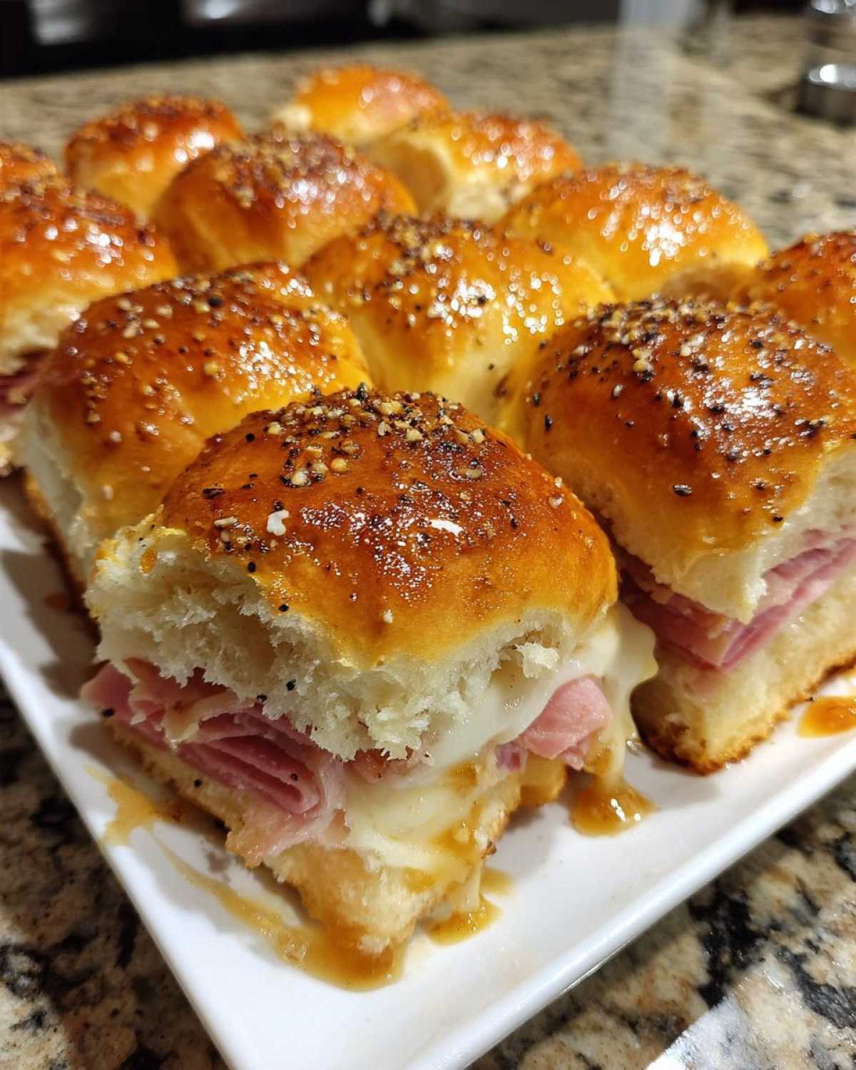 A tray of freshly baked Hawaiian Roll Ham and Cheese Sliders topped with a savory glaze and seeds.