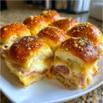 Close-up of gooey Hawaiian Roll Ham and Cheese Sliders with melted cheese oozing out, topped with seasoning.