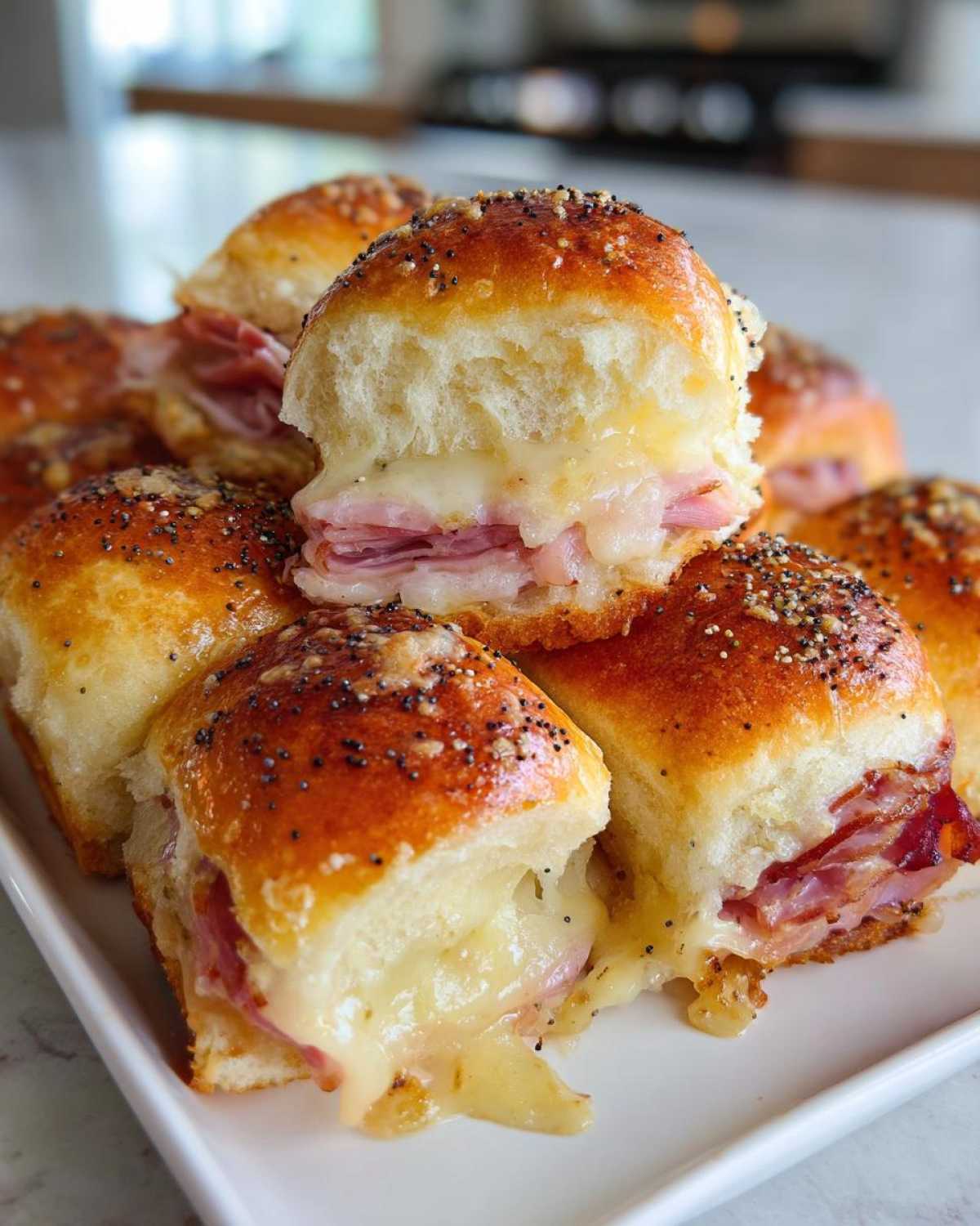Close-up of gooey Hawaiian Roll Ham and Cheese Sliders stacked, showing melted cheese oozing out.