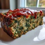 A thick slice of Healthy Turkey Spinach Meatloaf topped with a drizzle of ketchup, sitting on a white plate.