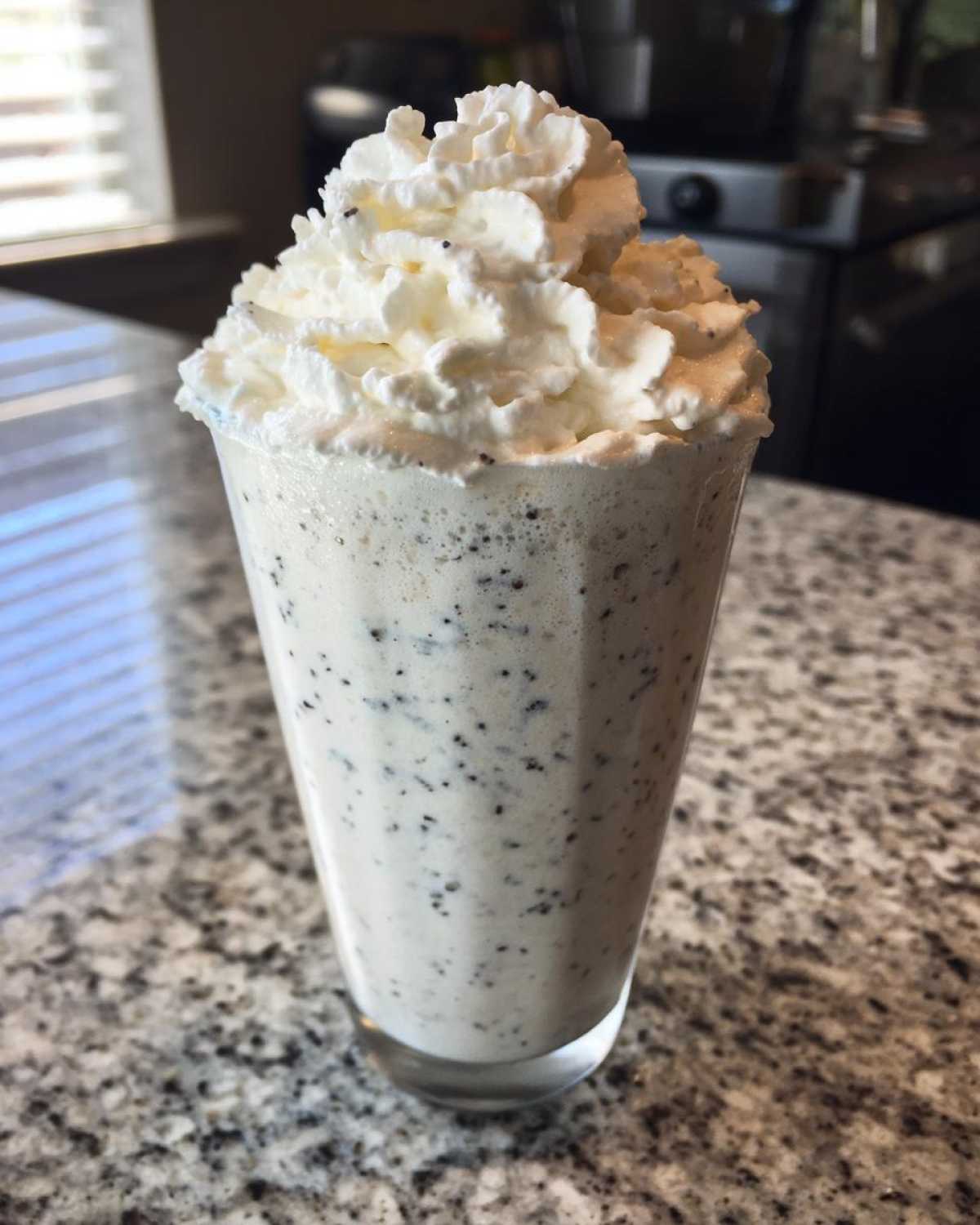 A tall glass of Homemade Vanilla Bean Frappuccino topped with a swirl of whipped cream and vanilla bean specks.