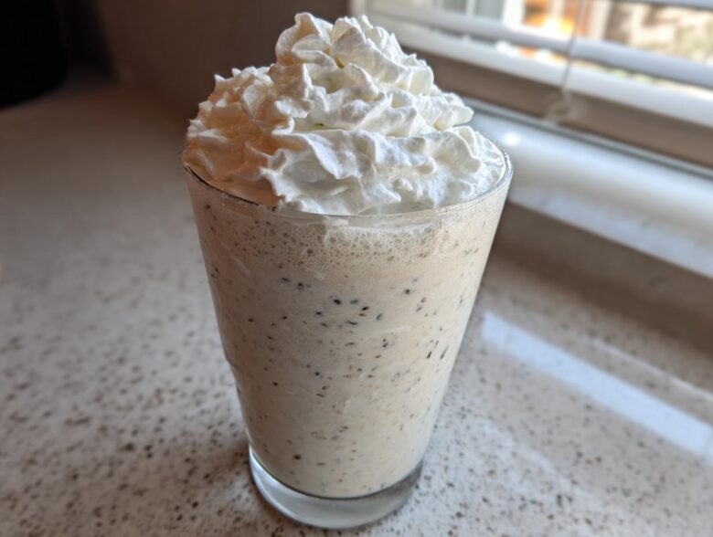 A tall glass of Homemade Vanilla Bean Frappuccino topped high with whipped cream, showing vanilla bean specks.