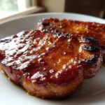 Two glistening Honey Glazed Ham Steak pieces served on a white plate, showing a caramelized, sticky coating.