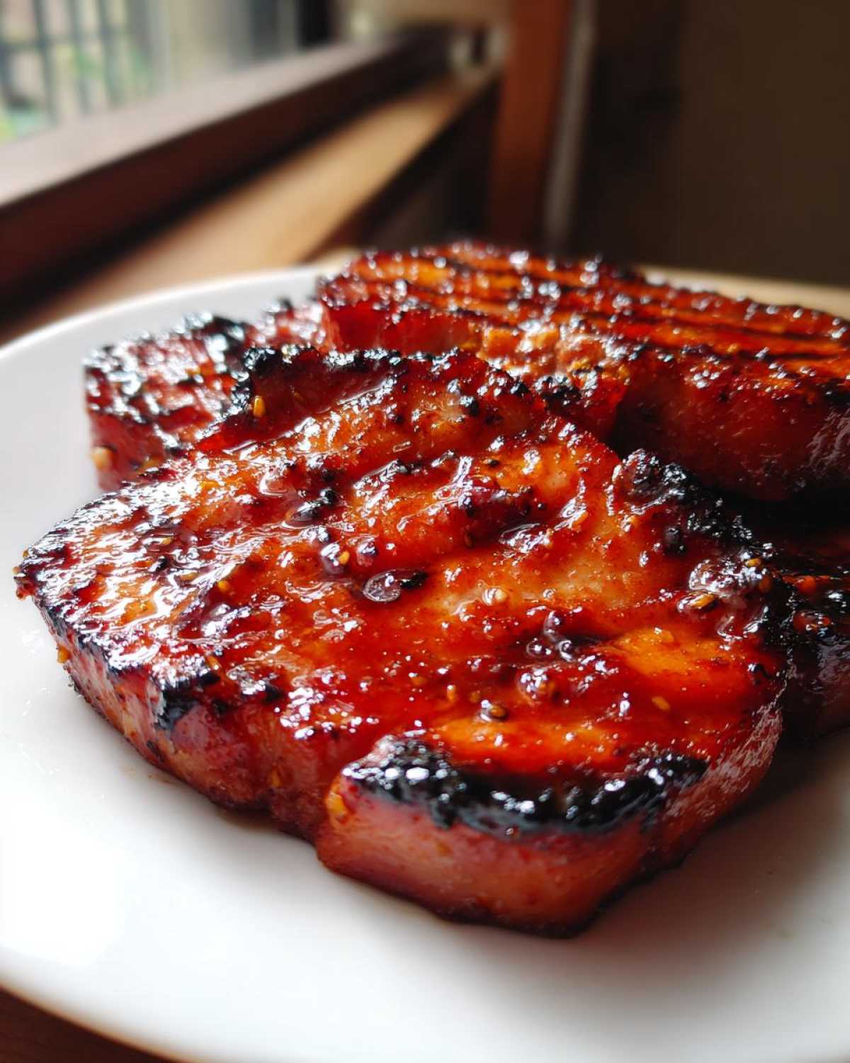 Close-up of thick, caramelized Honey Glazed Ham Steak slices glistening with a sweet, dark glaze on a white plate.