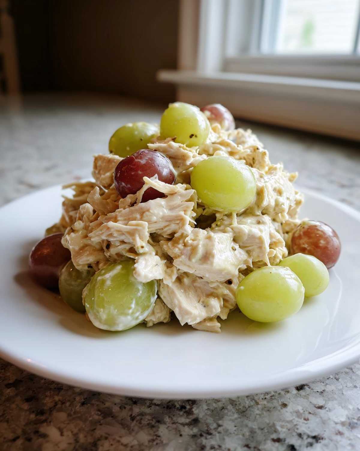 A mound of creamy Honey Mustard Chicken Salad with Grapes, featuring shredded chicken and whole red and green grapes, served on a white plate.