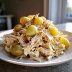 A mound of creamy Honey Mustard Chicken Salad with Grapes served on a white plate, highlighted by natural light.