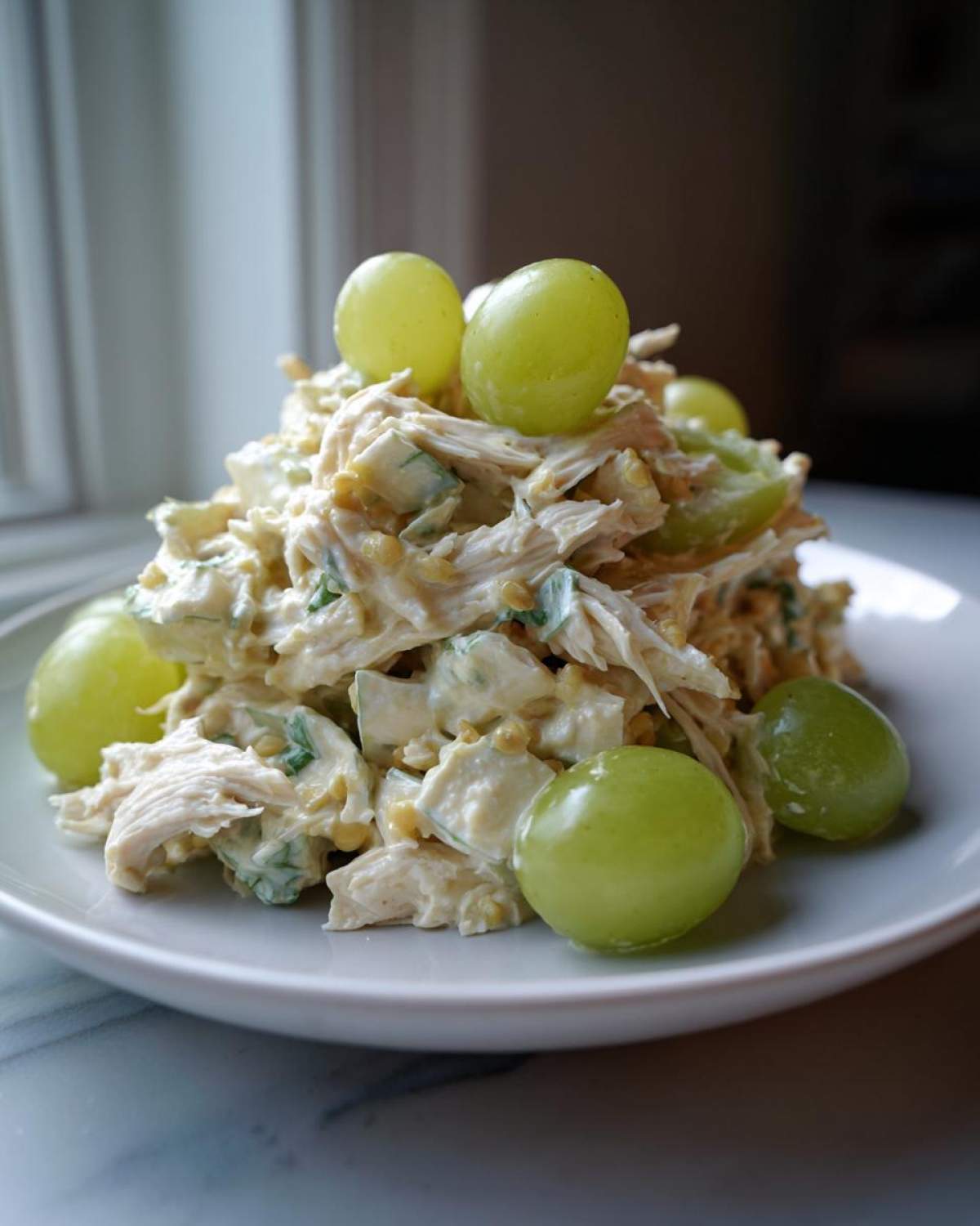 A mound of creamy Honey Mustard Chicken Salad with Grapes, garnished with whole green grapes, served on a white plate.