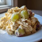 A mound of creamy Honey Mustard Chicken Salad with Grapes served on a white plate, highlighted by natural light.