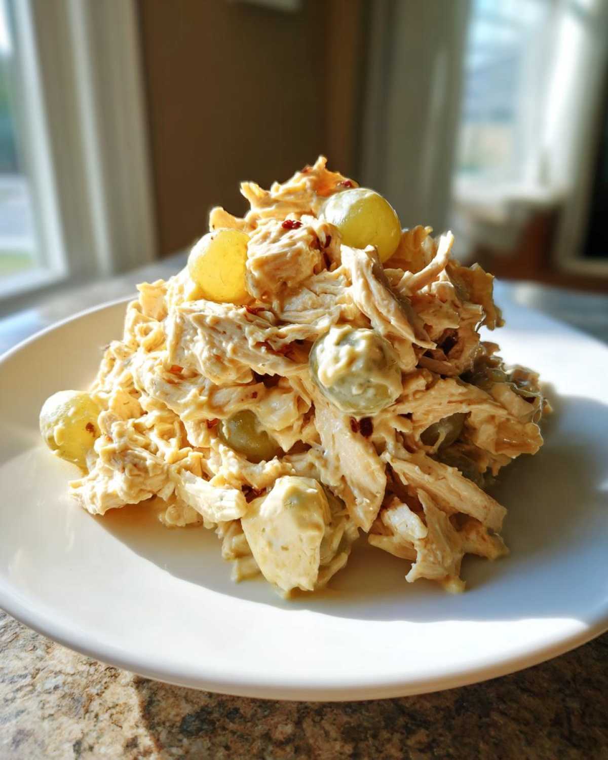 A mound of creamy Honey Mustard Chicken Salad with Grapes served on a white plate, brightly lit by natural window light.