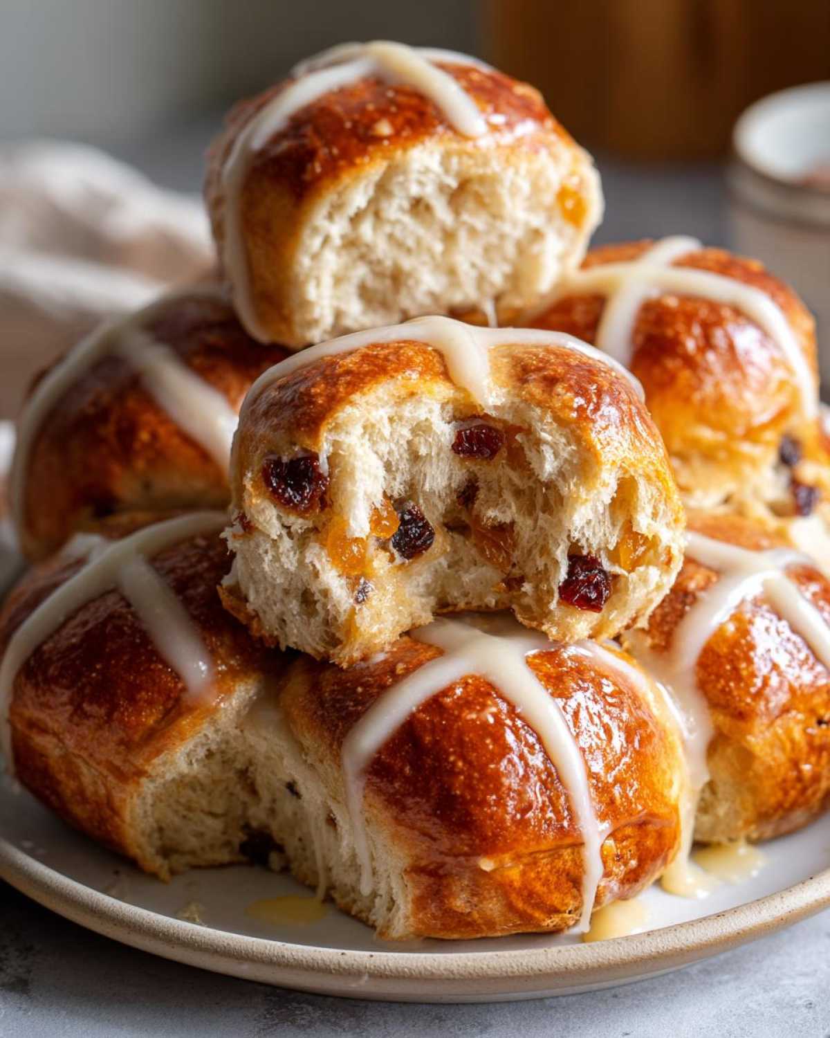 A stack of fluffy Hot Cross Buns with Orange Glaze, one bun broken open showing raisins inside.