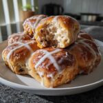 A stack of freshly baked Hot Cross Buns with Orange Glaze, featuring a white icing cross and a glossy sheen.