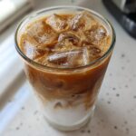 Close-up of a tall glass containing an Iced Honey Almond Milk Latte with distinct layers of white almond milk and rich brown coffee.