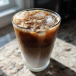 A tall glass of Iced Lavender Latte showing layers of milk and espresso over ice cubes.