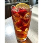 A tall glass filled with Iced Strawberry Lemon Tea, ice, sliced strawberries, and a lemon wheel garnish.