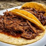 Close-up of two soft corn tortillas filled generously with shredded, saucy Instant Pot Beef Barbacoa.