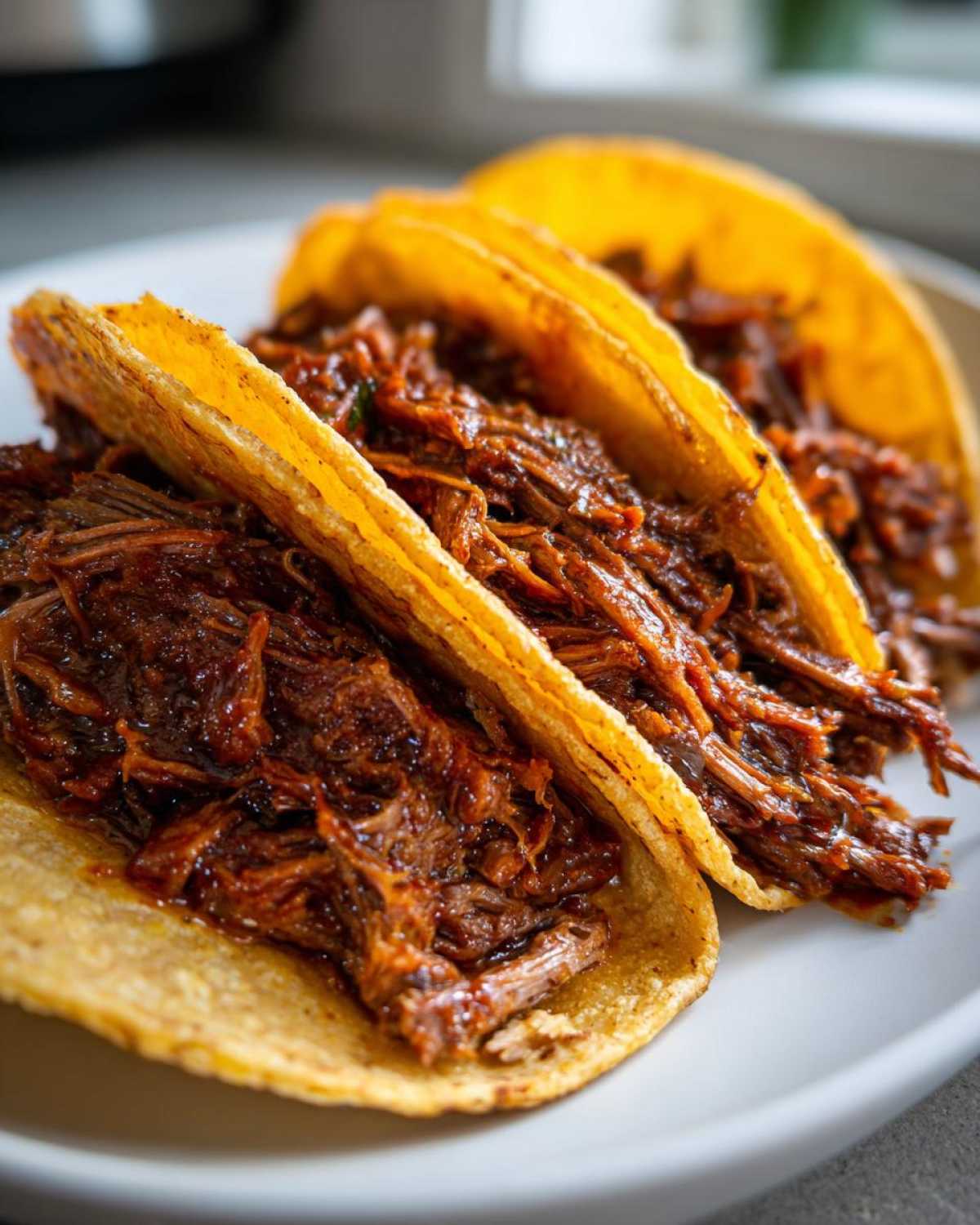 Close-up of three crispy tacos filled generously with shredded Instant Pot Beef Barbacoa.