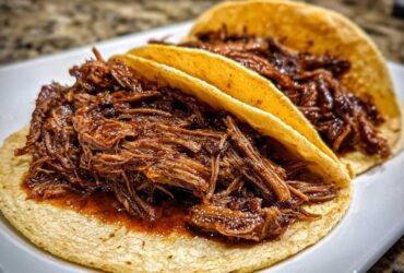 Close-up of two soft corn tortillas filled generously with shredded, saucy Instant Pot Beef Barbacoa.