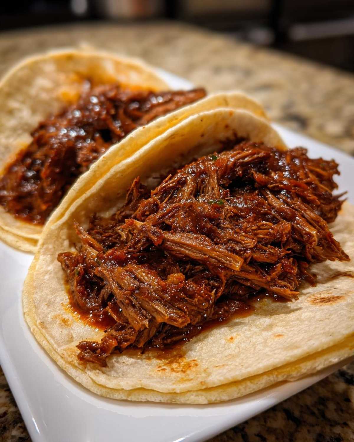 Two soft corn tortillas filled generously with shredded, saucy Instant Pot Beef Barbacoa for tacos.