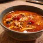 Close-up of a hearty bowl of Instant Pot Chicken Tortilla Soup with shredded chicken, tomatoes, and black beans.