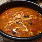 Close-up of rich, red broth Instant Pot Chicken Tortilla Soup with shredded chicken and black beans.