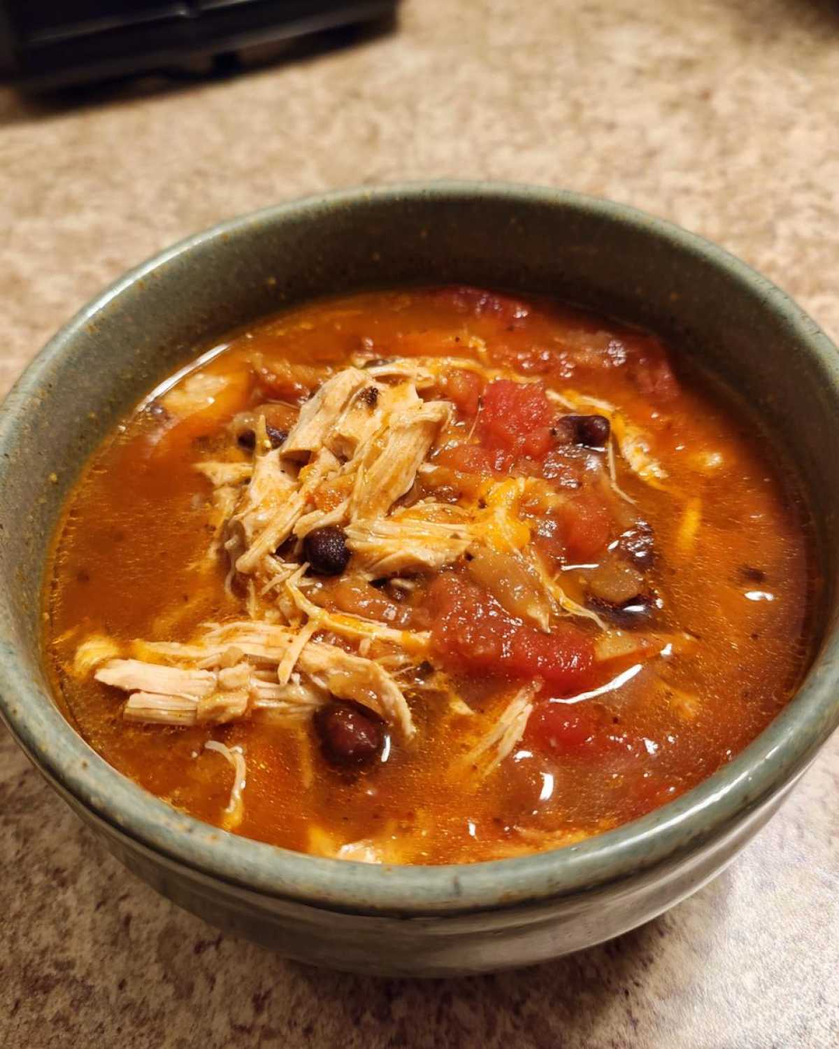 Close-up of a bowl of Instant Pot Chicken Tortilla Soup topped with shredded chicken and tomatoes.
