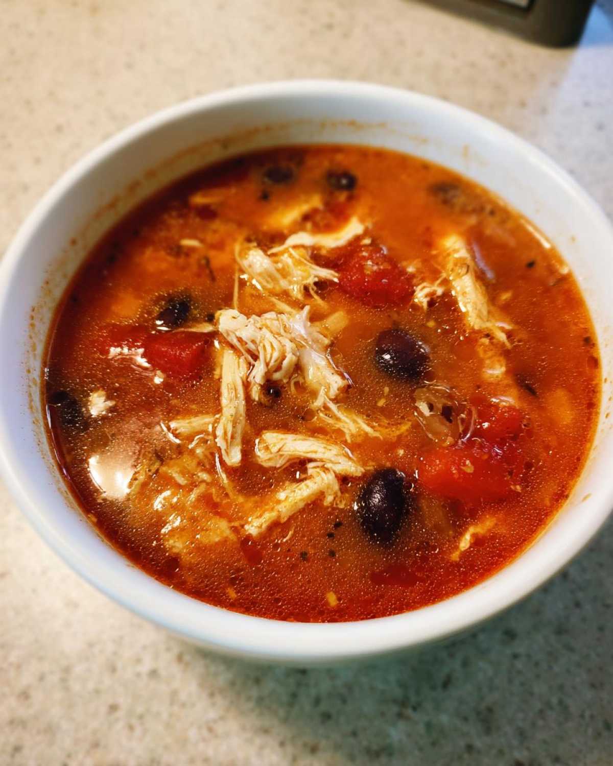 Close-up of a white bowl filled with rich, red Instant Pot Chicken Tortilla Soup featuring shredded chicken and black beans.