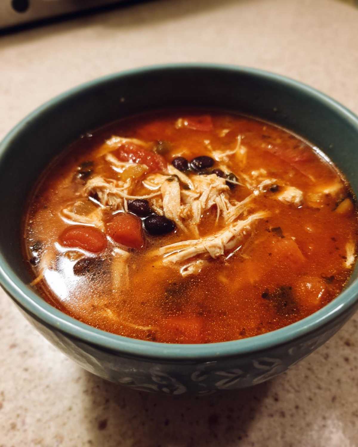 Close-up of a teal bowl filled with rich, red Instant Pot Chicken Tortilla Soup, featuring shredded chicken and black beans.