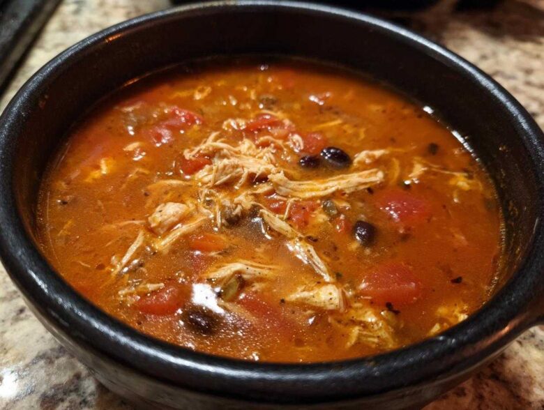 Close-up of rich, red broth Instant Pot Chicken Tortilla Soup with shredded chicken and black beans.