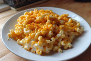 A close-up of creamy, cheesy Instant Pot Mac and Cheese topped with melted cheddar cheese on a white plate.