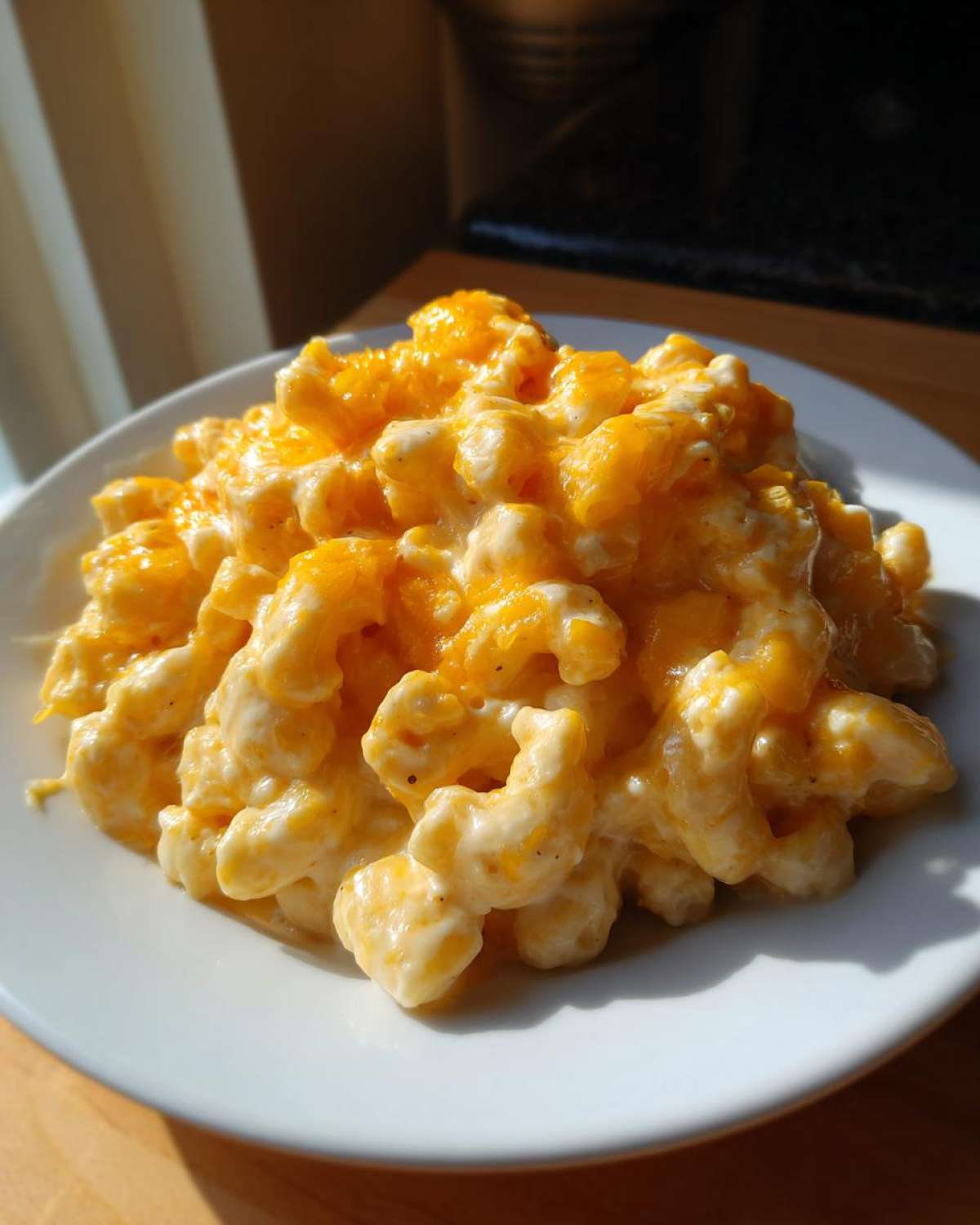 A close-up of creamy, cheesy Instant Pot Mac and Cheese piled high on a white plate, bathed in sunlight.