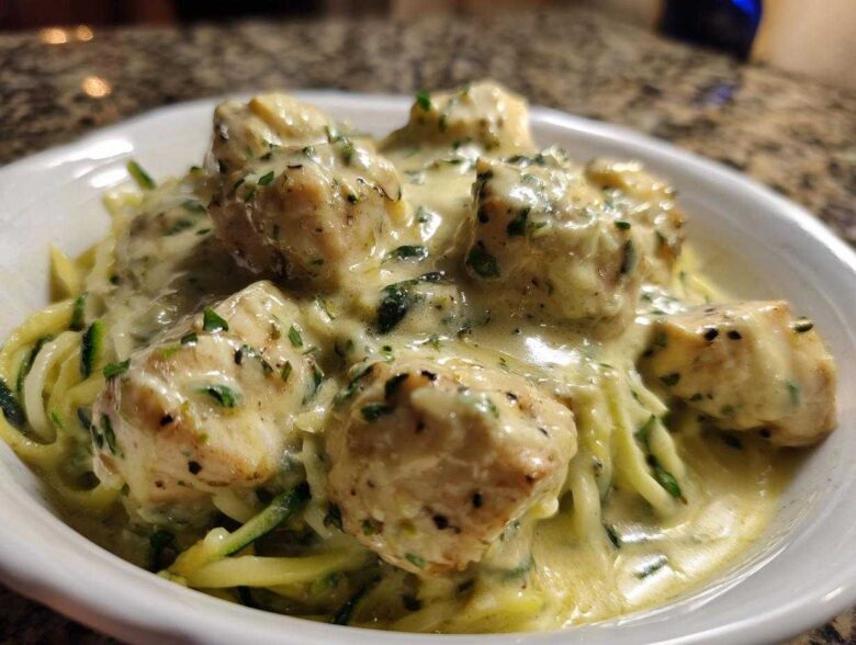 Close-up of Keto Chicken Alfredo featuring chunks of chicken breast smothered in creamy sauce over zucchini noodles.