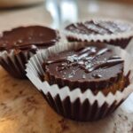 Three homemade Keto Chocolate Peanut Butter Fat Bombs in white paper liners, topped with sea salt.