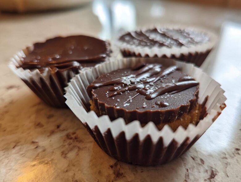 Three homemade Keto Chocolate Peanut Butter Fat Bombs in white paper liners, topped with sea salt.